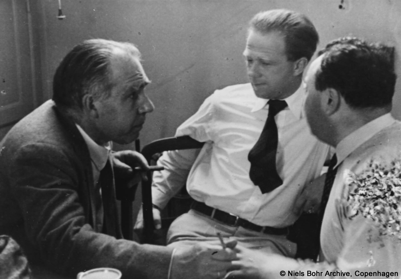 Wolfgang Pauli sitzt diskutierend mit Niels Bohr und Werner Heisenberg zusammen