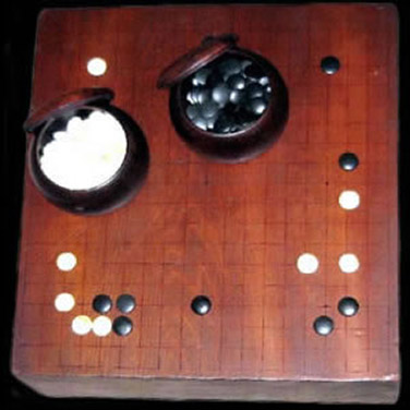 Two bowls on a brown playing field. In and around the bowls there are black and white game pieces