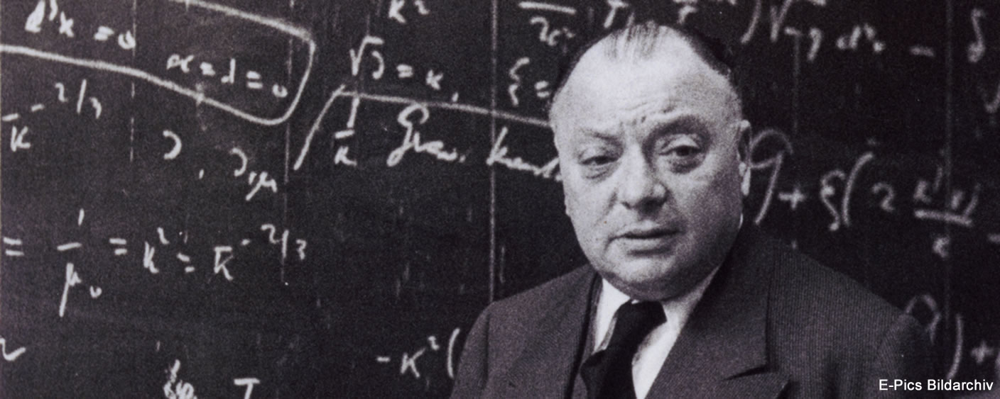 Wolfgang Pauli in front of a labelled wall chart