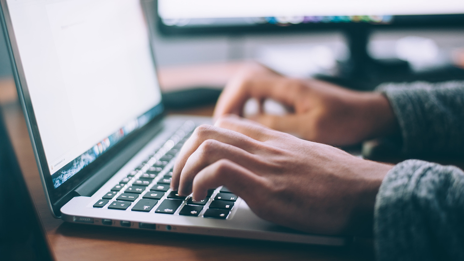 Hände auf Laptoptastatur mit externem Bildschirm im Hintergrund