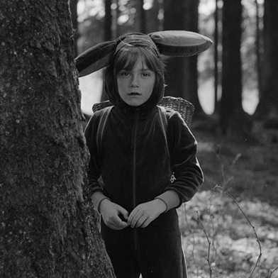 Ein Kind mit Hasenohren aus Stoff steht im Wald