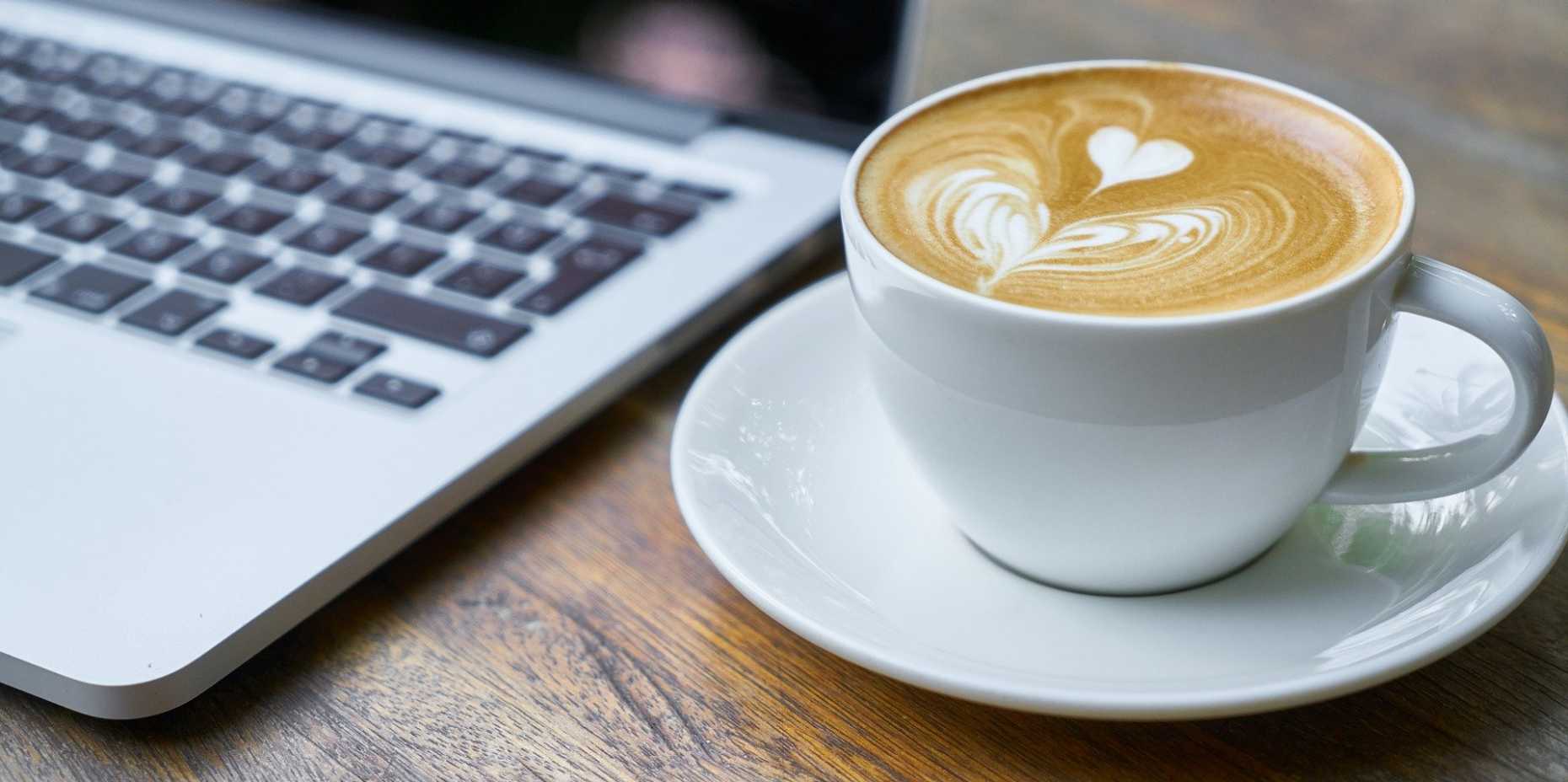 Kaffeetasse auf Holztisch neben MacBook